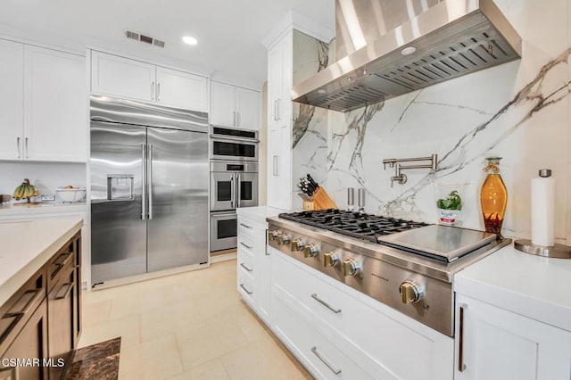 kitchen featuring backsplash, wall chimney range hood, stainless steel appliances, and white cabinetry