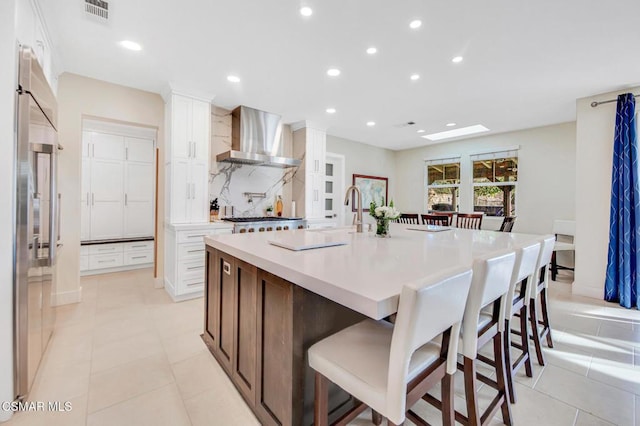 kitchen with white cabinets, a large island with sink, wall chimney exhaust hood, and a kitchen bar