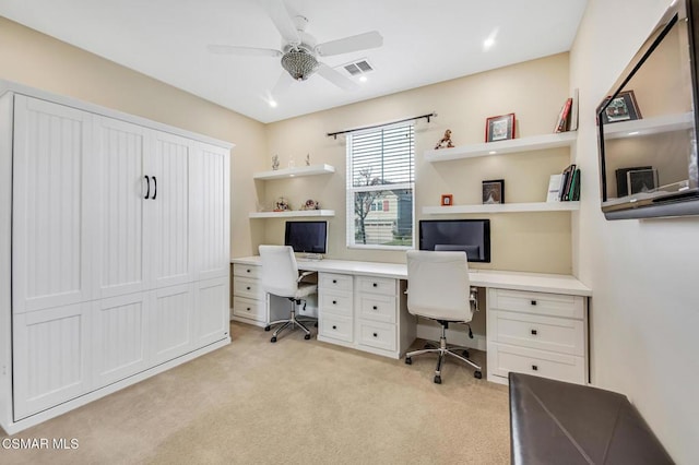 carpeted office space with built in desk and ceiling fan