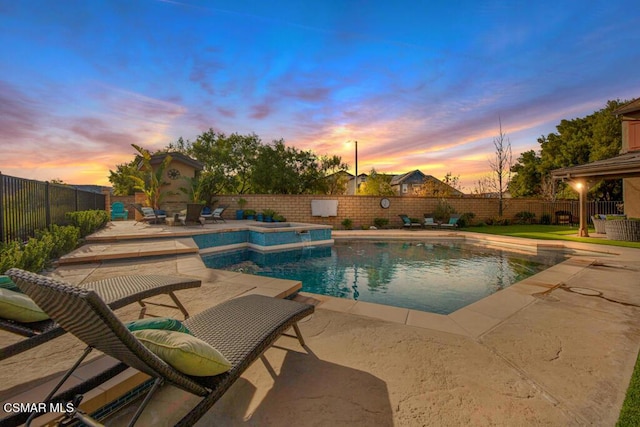 pool at dusk with a patio area and a hot tub