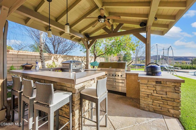 view of patio / terrace featuring a gazebo, an outdoor kitchen, exterior bar, ceiling fan, and grilling area