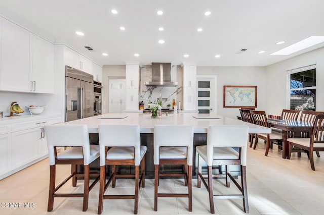 kitchen with stainless steel appliances, wall chimney exhaust hood, a large island with sink, and a breakfast bar