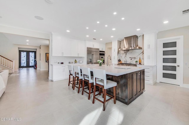 kitchen with white cabinetry, a large island, built in refrigerator, a kitchen breakfast bar, and wall chimney range hood