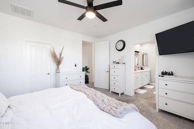 bedroom featuring ceiling fan, ensuite bathroom, and light colored carpet