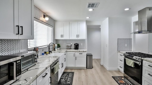 kitchen featuring wall chimney exhaust hood, light stone counters, stainless steel appliances, and white cabinetry