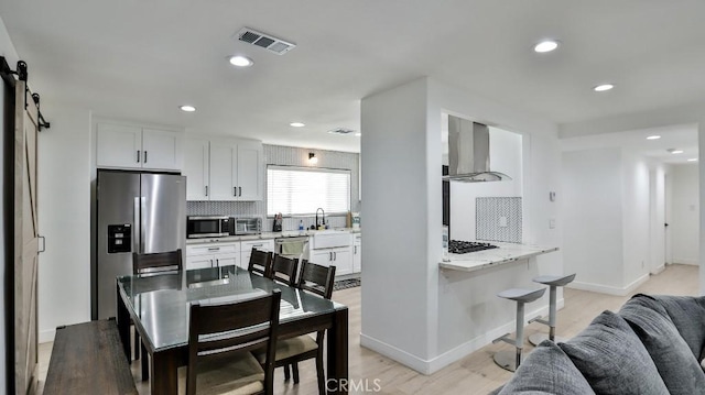 kitchen with white cabinets, kitchen peninsula, wall chimney range hood, and stainless steel appliances