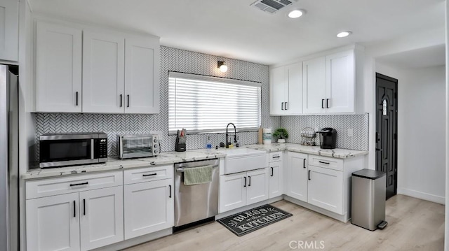 kitchen with white cabinetry, stainless steel appliances, light wood-type flooring, light stone countertops, and sink