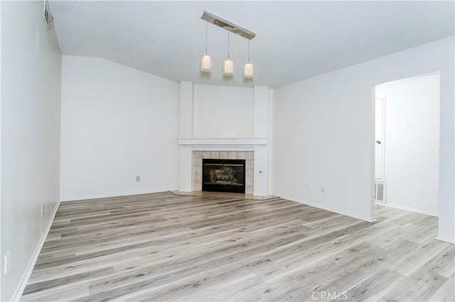 unfurnished living room featuring light wood-type flooring, a textured ceiling, a tile fireplace, and rail lighting