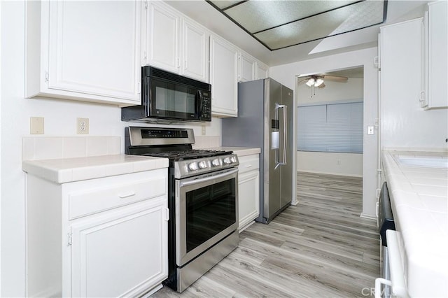 kitchen featuring appliances with stainless steel finishes, tile counters, white cabinetry, light hardwood / wood-style floors, and sink