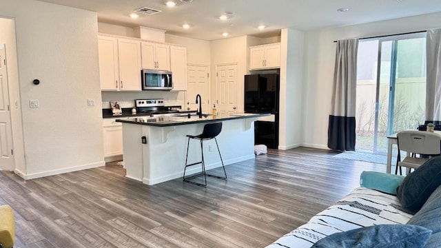 kitchen with white cabinetry, a center island with sink, hardwood / wood-style flooring, a kitchen breakfast bar, and stove