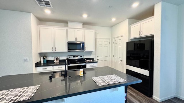 kitchen with sink, white cabinetry, appliances with stainless steel finishes, dark hardwood / wood-style floors, and a kitchen island with sink