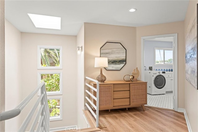 laundry area featuring washer and clothes dryer, light hardwood / wood-style flooring, and a skylight