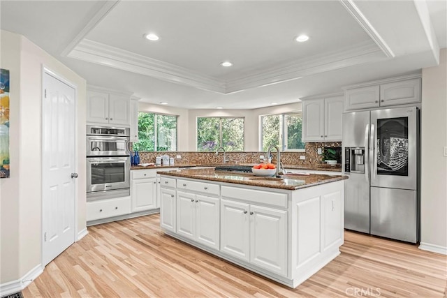 kitchen featuring a center island with sink, stainless steel appliances, tasteful backsplash, a tray ceiling, and white cabinets