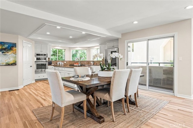 dining space featuring light hardwood / wood-style floors, sink, and a raised ceiling