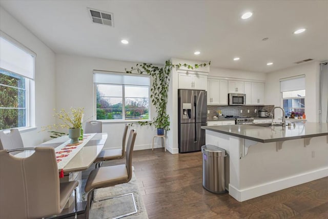 kitchen with appliances with stainless steel finishes, a kitchen bar, white cabinetry, sink, and dark hardwood / wood-style floors