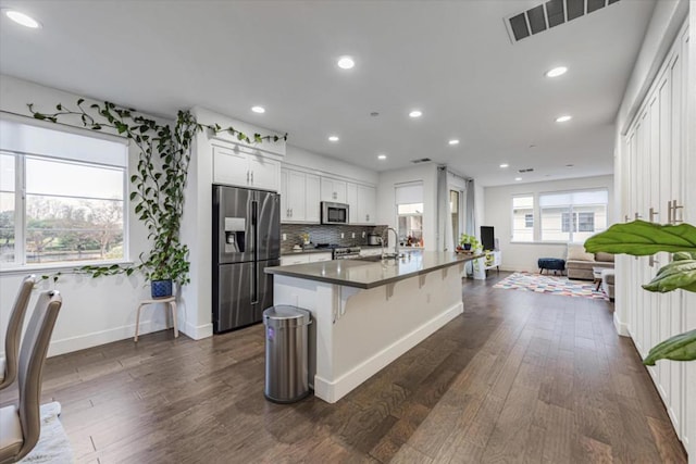 kitchen with a kitchen bar, white cabinetry, dark wood-type flooring, appliances with stainless steel finishes, and an island with sink