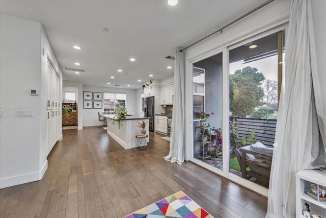 kitchen with white cabinetry, a center island with sink, a kitchen breakfast bar, dark wood-type flooring, and stainless steel refrigerator