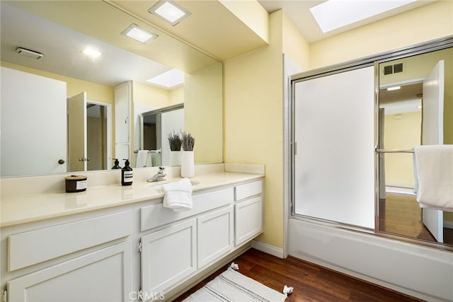 bathroom with bath / shower combo with glass door, a skylight, hardwood / wood-style floors, and vanity