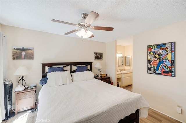 bedroom featuring ceiling fan, light hardwood / wood-style floors, ensuite bath, sink, and a textured ceiling