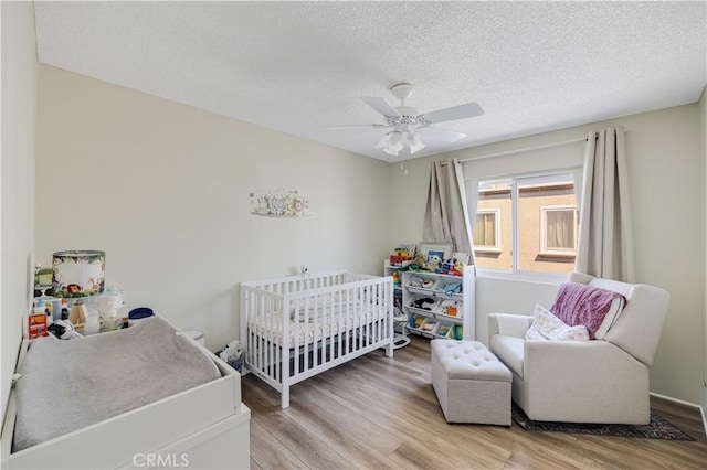 bedroom with light wood-type flooring, ceiling fan, a textured ceiling, and a nursery area