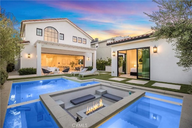 back house at dusk with a pool with hot tub, an outdoor living space with a fire pit, and a patio area