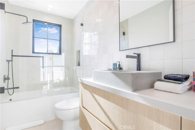 full bathroom with toilet, bath / shower combo with glass door, tile walls, vanity, and tile patterned flooring