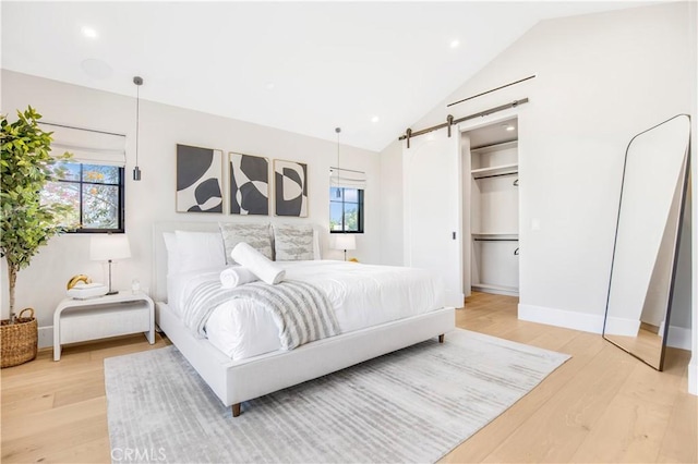 bedroom with lofted ceiling, a barn door, multiple windows, and hardwood / wood-style floors