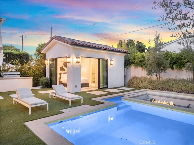 back house at dusk featuring a lawn and an outdoor structure