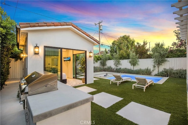 back house at dusk featuring a fenced in pool, exterior kitchen, a yard, and a patio