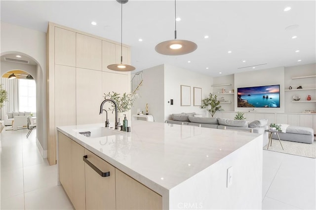 kitchen with sink, hanging light fixtures, built in features, light stone counters, and a center island with sink