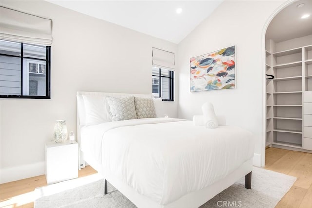 bedroom with vaulted ceiling, a walk in closet, and light hardwood / wood-style flooring