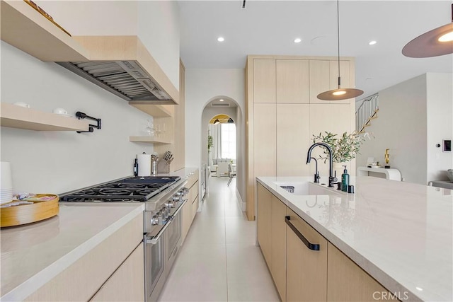 kitchen featuring stainless steel stove, light brown cabinets, hanging light fixtures, and sink