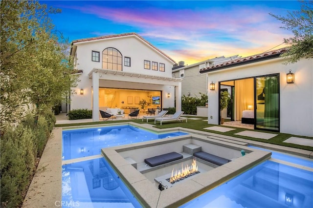 back house at dusk featuring a fire pit and an in ground hot tub