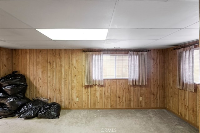 carpeted empty room with a drop ceiling, a wealth of natural light, and wooden walls