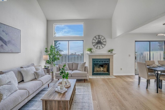 living room with a high ceiling, a wealth of natural light, a tiled fireplace, and light wood-type flooring