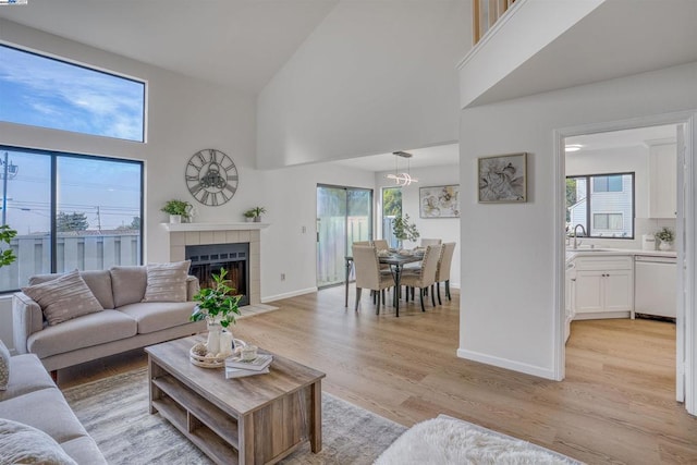 living room featuring a towering ceiling, light hardwood / wood-style flooring, a tile fireplace, and sink