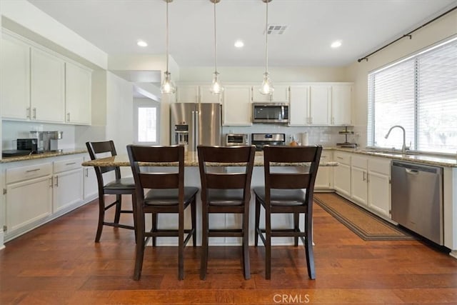 kitchen with decorative light fixtures, light stone countertops, stainless steel appliances, and a kitchen island