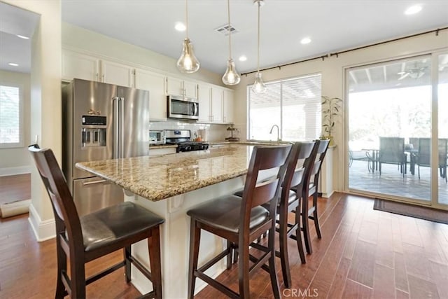 kitchen featuring pendant lighting, a kitchen bar, decorative backsplash, appliances with stainless steel finishes, and white cabinets