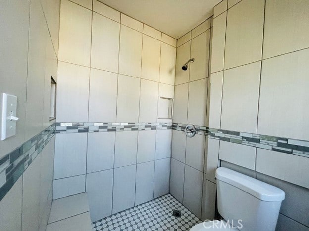 bathroom featuring toilet, tile walls, and tiled shower