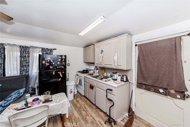 kitchen with light hardwood / wood-style flooring, white gas stove, white cabinetry, and black fridge