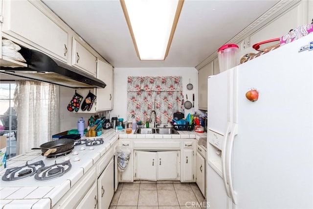 kitchen with tile counters, light tile patterned floors, sink, and white appliances