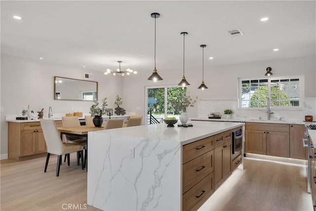 kitchen with hanging light fixtures, light wood-type flooring, a wealth of natural light, and tasteful backsplash