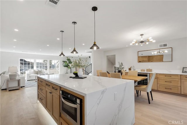 kitchen featuring decorative light fixtures, a spacious island, light hardwood / wood-style floors, an inviting chandelier, and stainless steel oven