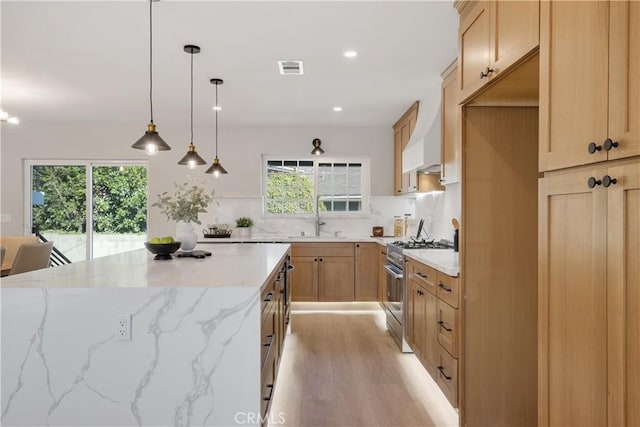 kitchen with high end stainless steel range oven, decorative light fixtures, light wood-type flooring, light stone counters, and sink