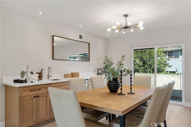 dining area with light wood-type flooring, an inviting chandelier, and sink