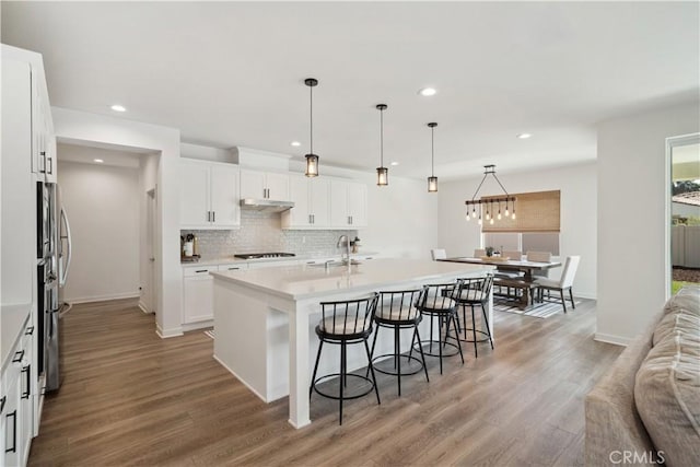 kitchen with sink, black stovetop, hanging light fixtures, an island with sink, and white cabinets