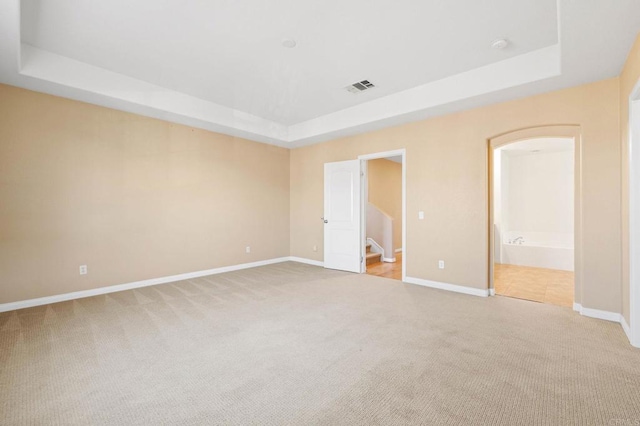 unfurnished bedroom featuring baseboards, visible vents, a raised ceiling, and light colored carpet