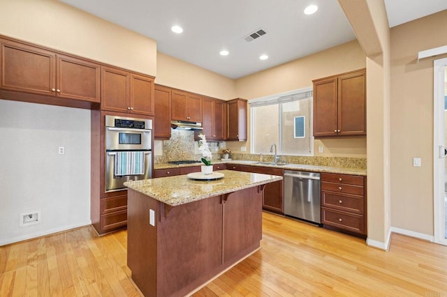 kitchen featuring light wood finished floors, visible vents, light stone counters, a center island, and stainless steel appliances