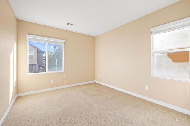 empty room featuring light carpet, visible vents, and baseboards