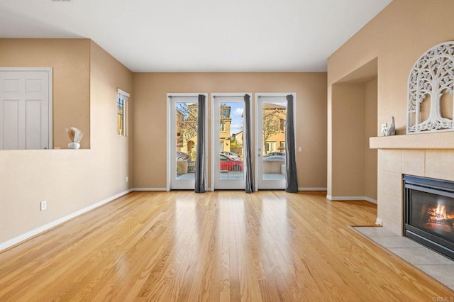 unfurnished living room with light wood-style floors, baseboards, and a tiled fireplace